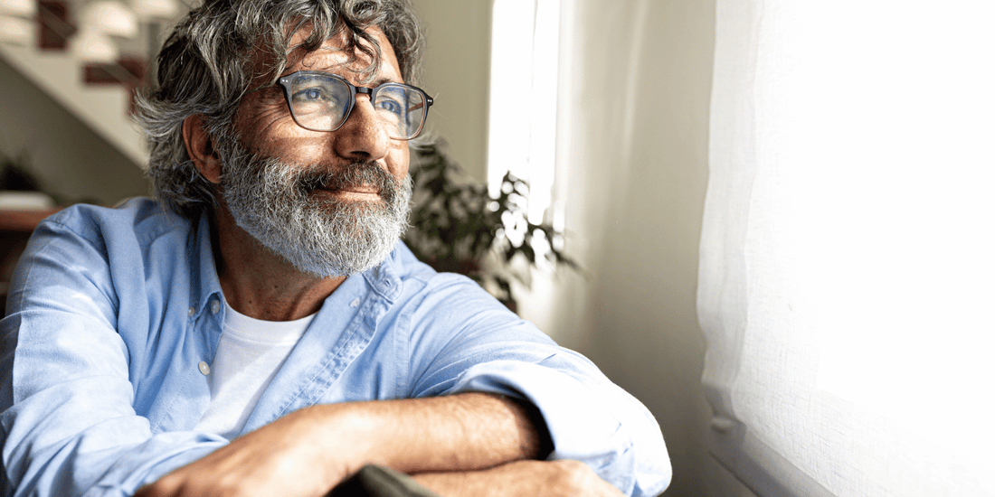 A man with a beard and glasses is seated on a couch, appearing relaxed.
