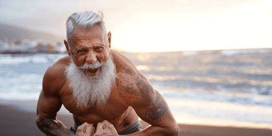 An older man with a white beard and hair looks thrilled on the beach, showcasing his strength and enthusiasm for life.