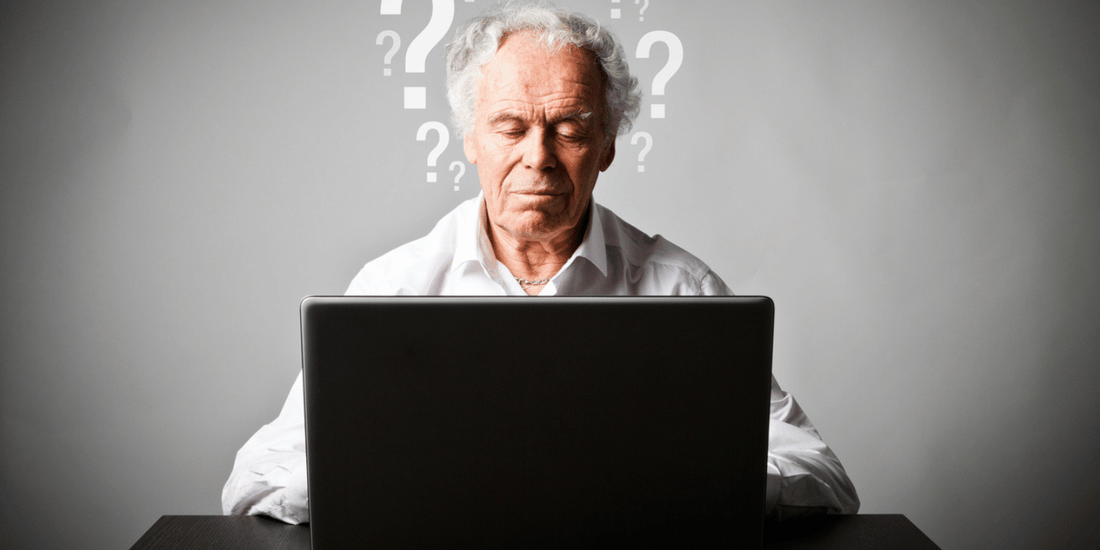 An older man sits at a desk, focused on his laptop.