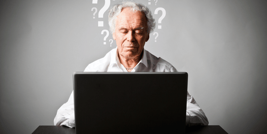 An older man sits at a desk, focused on his laptop.