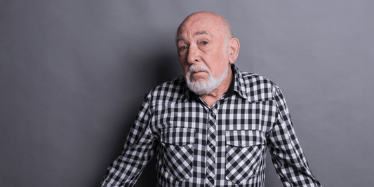 An older gentleman with a beard, sporting a checkered shirt, looking thoughtfully into the distance.