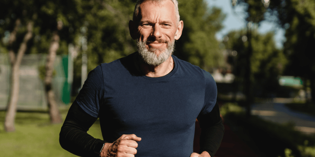 A bearded man jogging through a green park, surrounded by trees and sunlight.