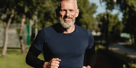  A bearded man jogging through a green park, surrounded by trees and sunlight.