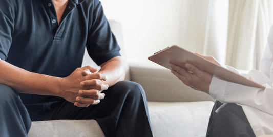 A man and a doctor engage in conversation while seated on a couch in a clinical setting.