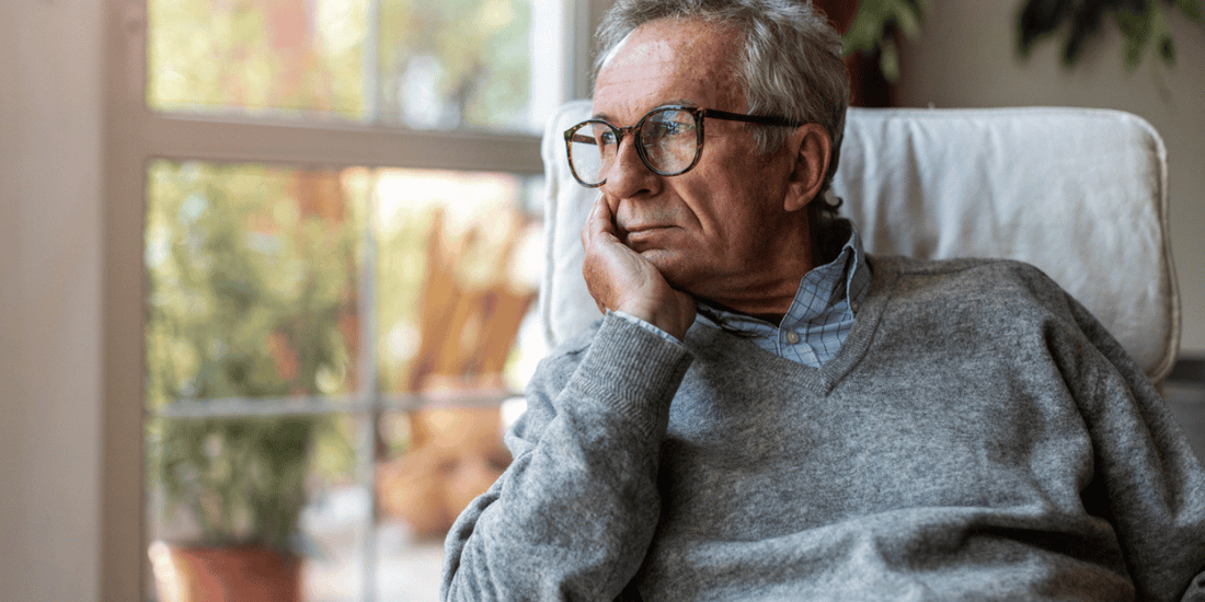 An elderly man seated in a chair, with his hand on his chin, appearing deep in thought or contemplation.