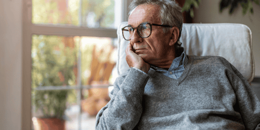 An elderly man seated in a chair, with his hand on his chin, appearing deep in thought or contemplation.