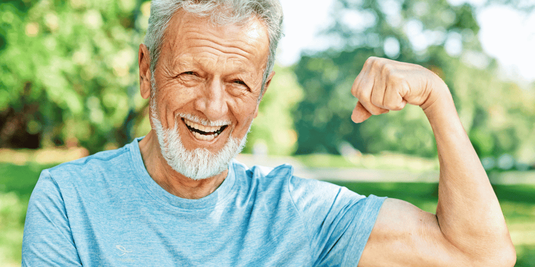  A senior man proudly displays his muscular physique by flexing, emphasizing his fitness and determination.