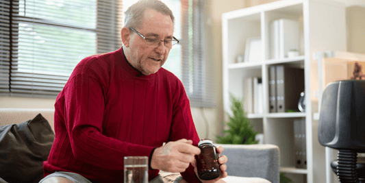 An older man sits on a couch, holding a glass of water, looking relaxed and contemplative.