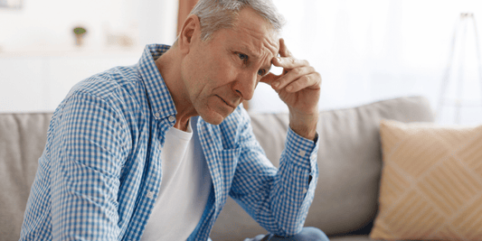 A man sitting on a couch, resting his hand on his head, appears deep in thought or contemplation.