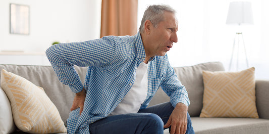 Elderly man on couch leaning over in pain holding his back