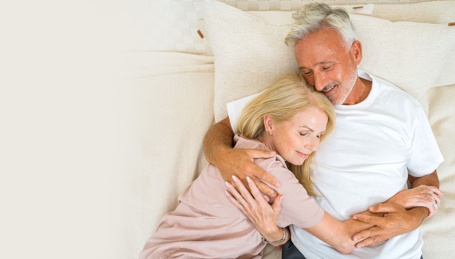 Couple holding onto each other tightly and smiling on a bed