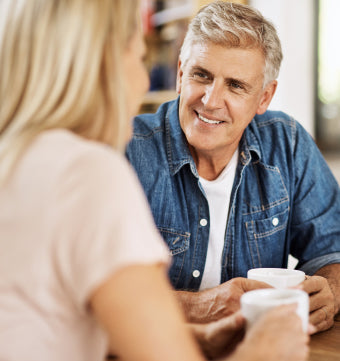 Man smiling while drinking coffee in kitchen with his wife